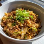 Close-up of a white bowl filled with savory egg roll in a bowl mixture of ground meat and cabbage, topped with fresh scallions.