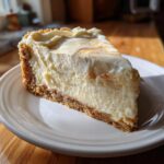 A perfect slice of creamy sugar cookie cheesecake with a thick graham cracker crust, sitting on a white plate.