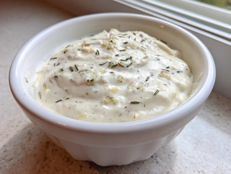 A close-up of thick, creamy homemade garlic sauce topped with herbs in a small white bowl.