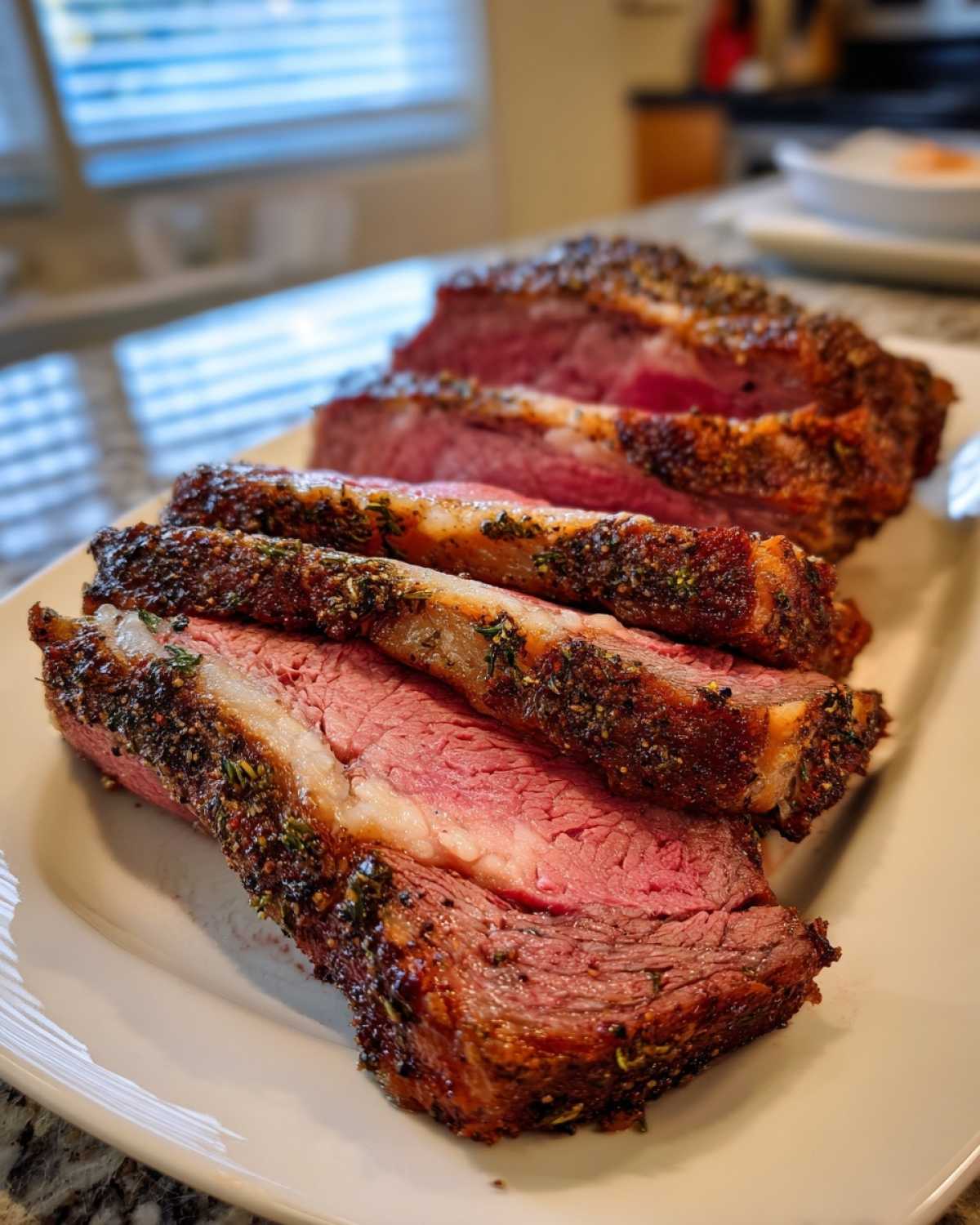 Close-up of thick slices of medium-rare rib roast with a dark, herbed crust on a white platter.