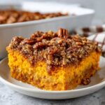 A close-up of a square serving of bright orange butternut squash casserole topped with a crunchy pecan streusel.