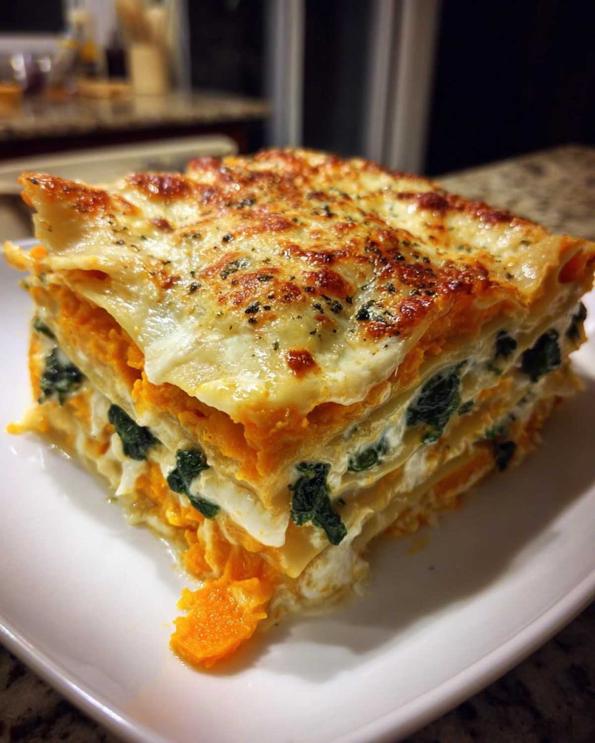 A thick, layered slice of butternut squash lasagna with spinach and a golden, bubbly cheese topping.