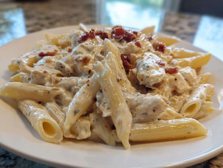 Close-up of a serving of chicken bacon ranch pasta featuring penne noodles coated in a creamy white sauce and topped with bacon bits.