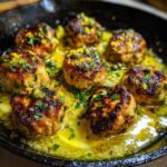 Close-up of seared chicken piccata meatballs simmering in a bright yellow lemon-butter sauce, garnished with capers and zest.