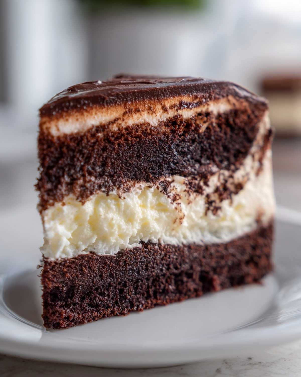 Close-up of a rich, layered slice of chocolate italian love cake featuring dark cake, white cream filling, and chocolate ganache.
