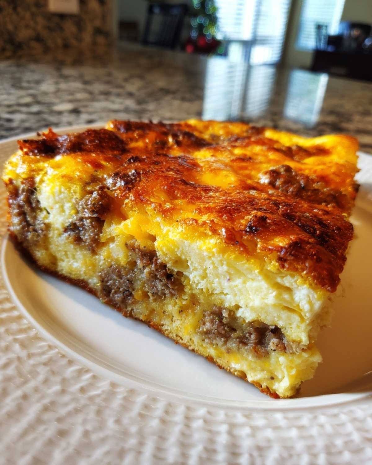 A thick slice of Christmas breakfast casserole featuring layers of egg, cheese, and sausage on a white plate.