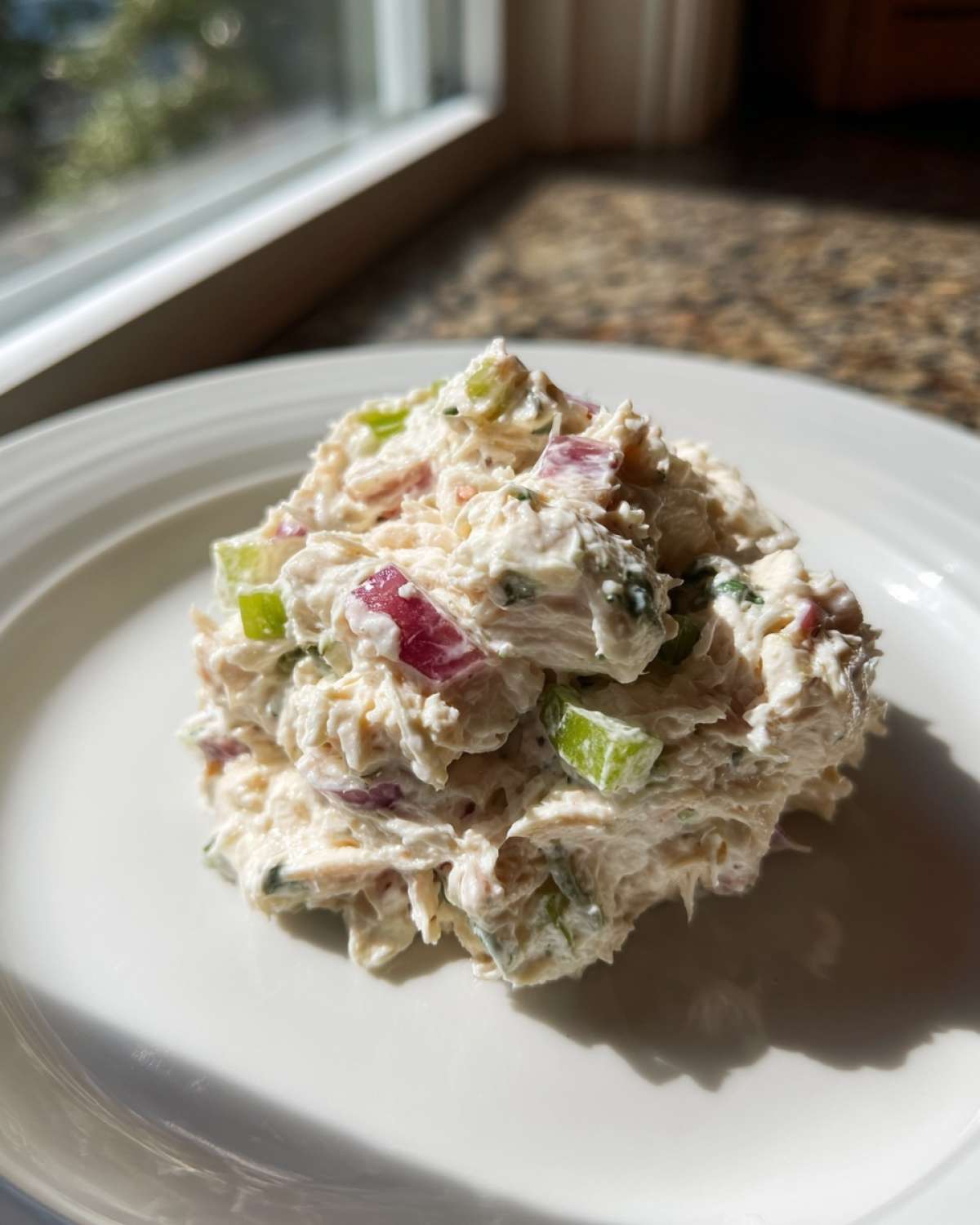A scoop of creamy cottage cheese chicken salad mixed with celery and red onion served on a white plate.