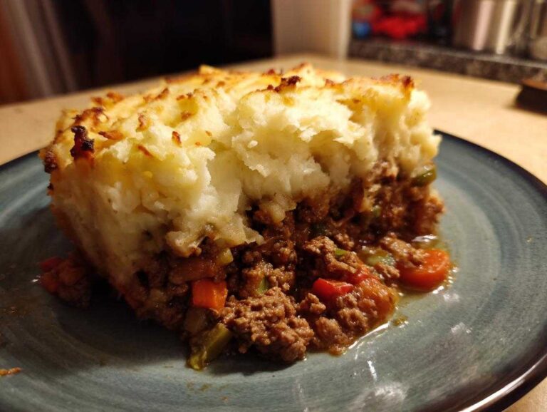 A thick slice of homemade cottage pie recipe showing rich meat filling and fluffy, browned mashed potato topping.