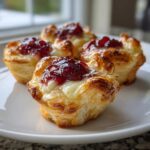 Close-up of four golden, flaky cranberry brie bites topped with melted brie and dark red cranberry sauce.