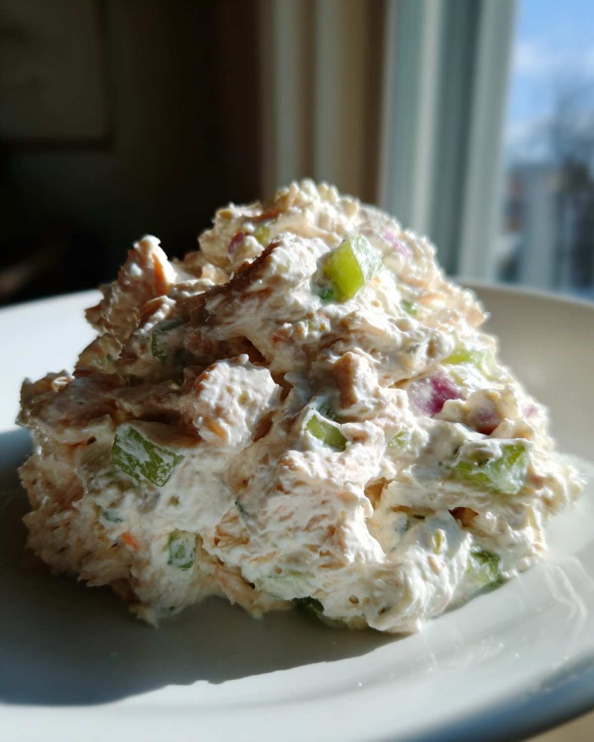 A scoop of creamy cottage cheese chicken salad featuring visible chunks of celery and red onion on a white plate.