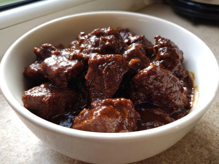 Close-up of tender crockpot beef tips coated in a thick, dark brown savory sauce in a white bowl.
