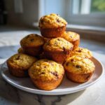 A stack of freshly baked, golden mini banana muffins dotted with chocolate chips on a white plate.
