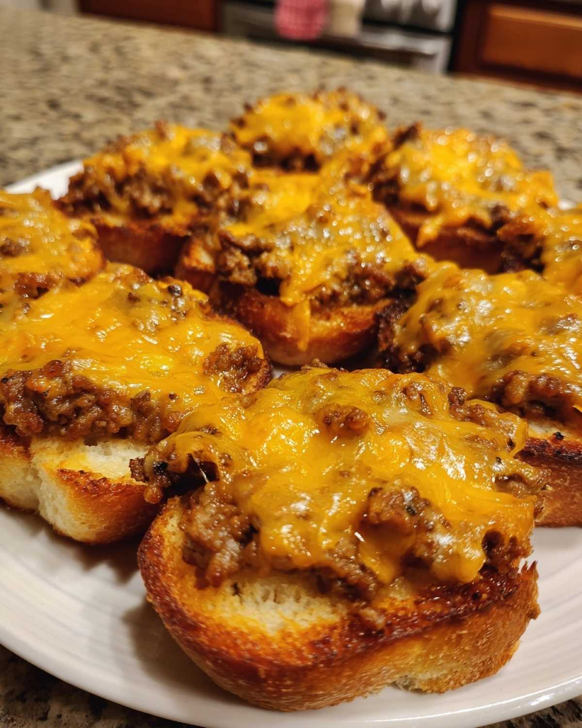 Close-up of several toasted bread rounds topped with savory meat mixture and melted cheddar cheese, ready to serve as hanky panky recipe appetizers.