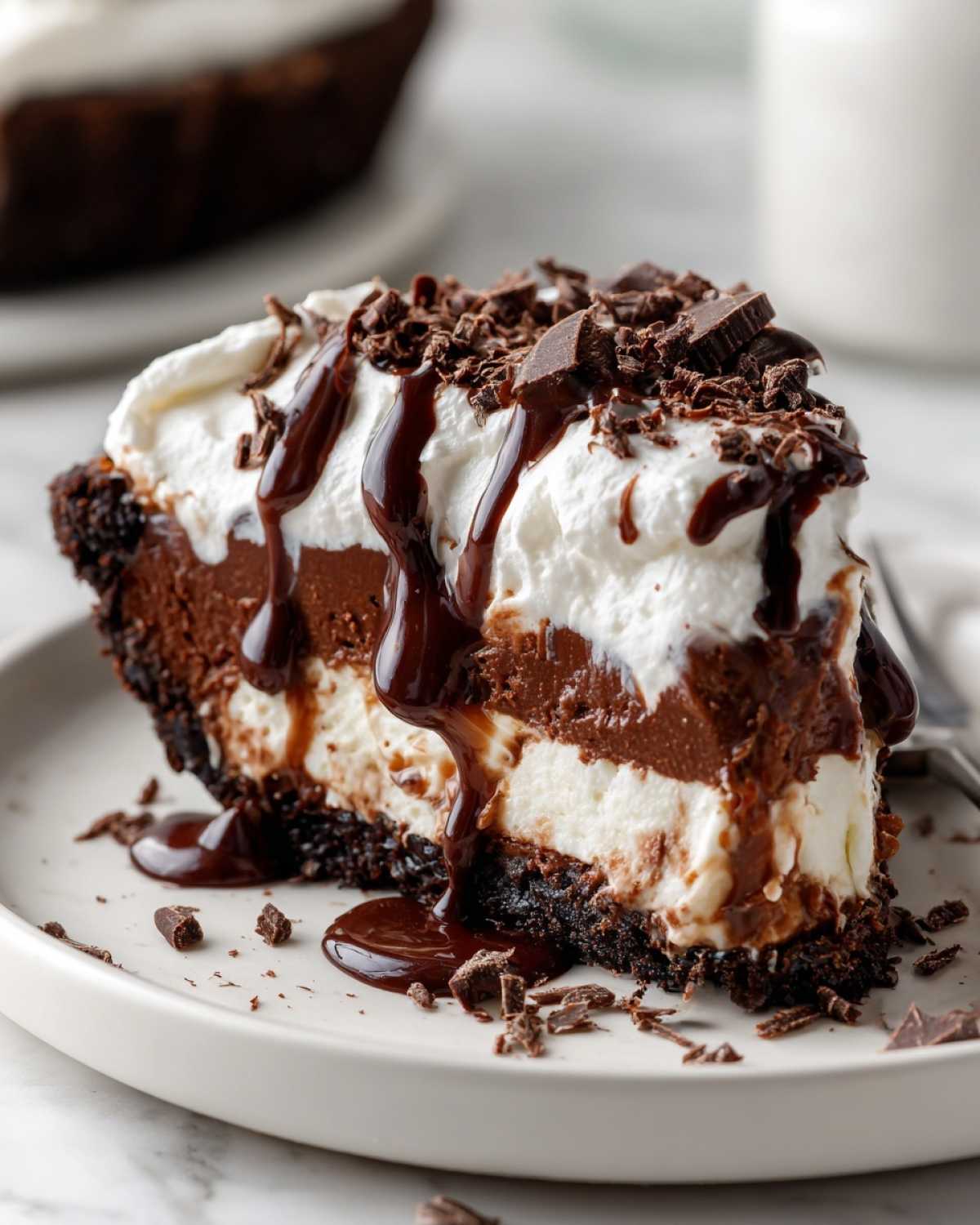 A rich slice of Mississippi Mud Pie featuring layers of chocolate, cream, and a chocolate cookie crust, topped with whipped cream and fudge.