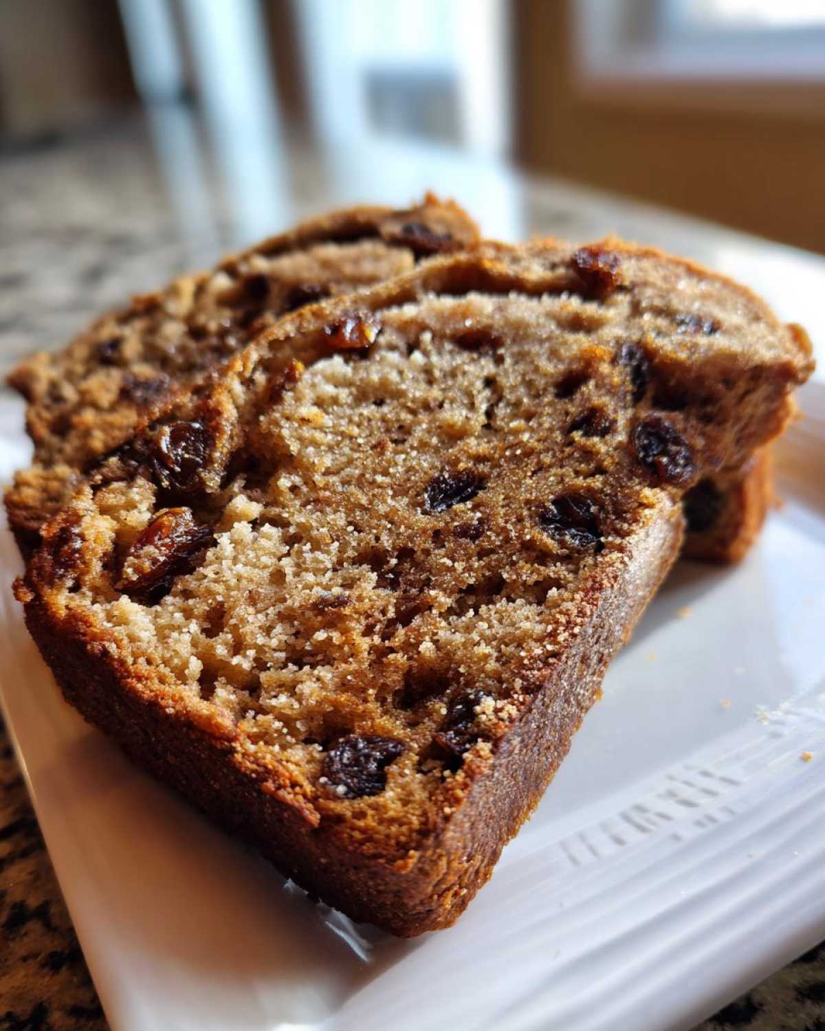 Two thick slices of moist, brown raisin bread resting on a white plate, showing visible raisins.