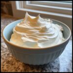 A light blue bowl filled with perfectly stiff, bright white royal icing recipe mixture.