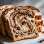 A thick slice of homemade raisin bread showing a beautiful cinnamon swirl and plump raisins throughout the soft crumb.