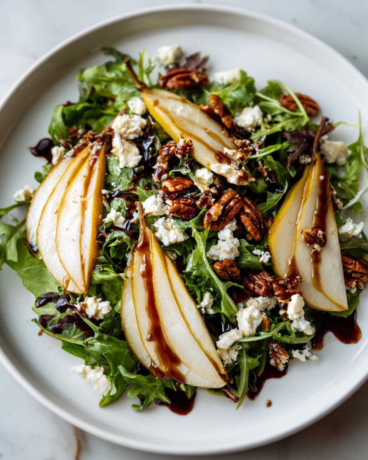 A vibrant pear salad featuring sliced pears, crumbled cheese, pecans, and a dark balsamic glaze over mixed greens.