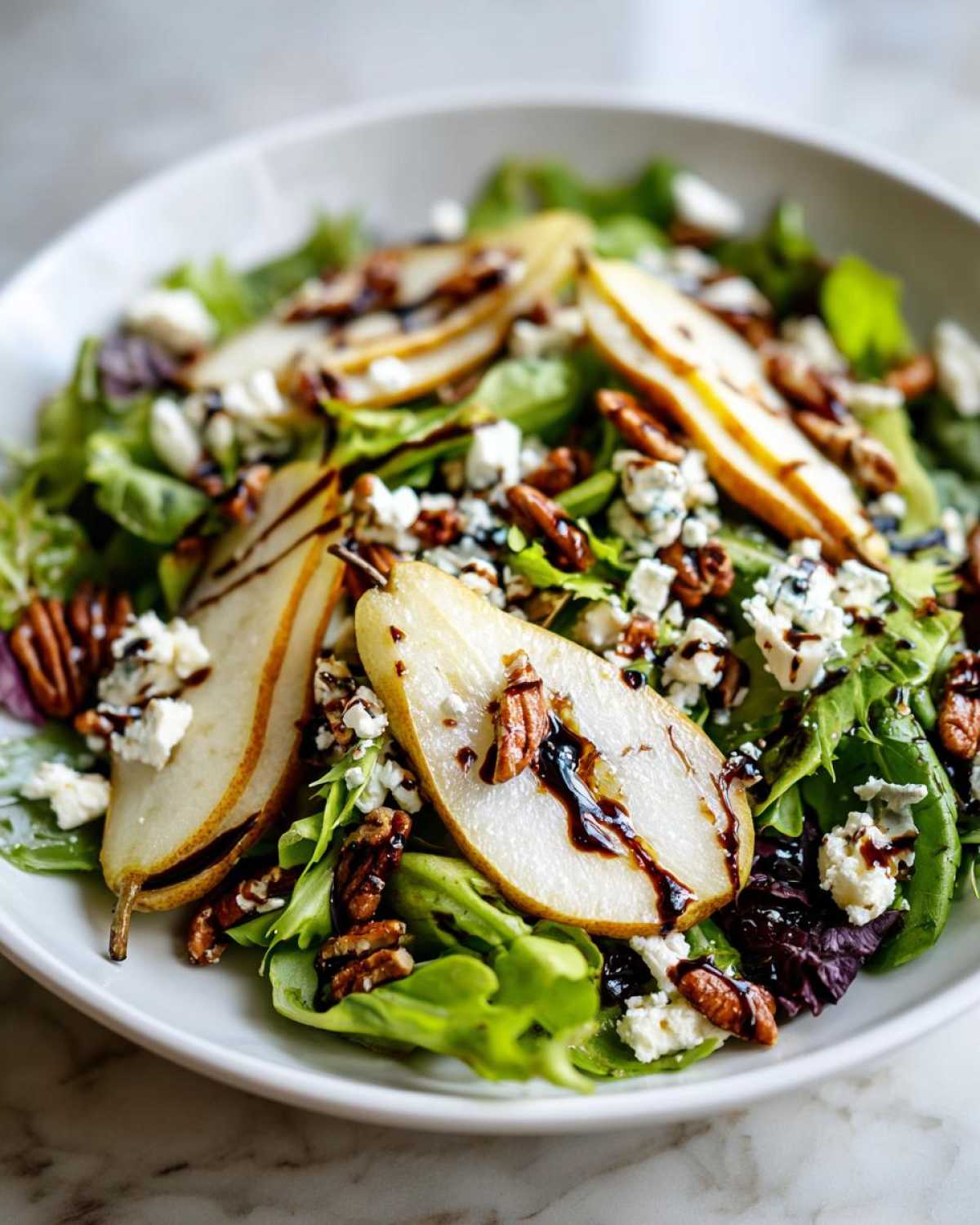 A close-up view of a vibrant pear salad featuring sliced pears, crumbled blue cheese, pecans, and a balsamic glaze over mixed greens.