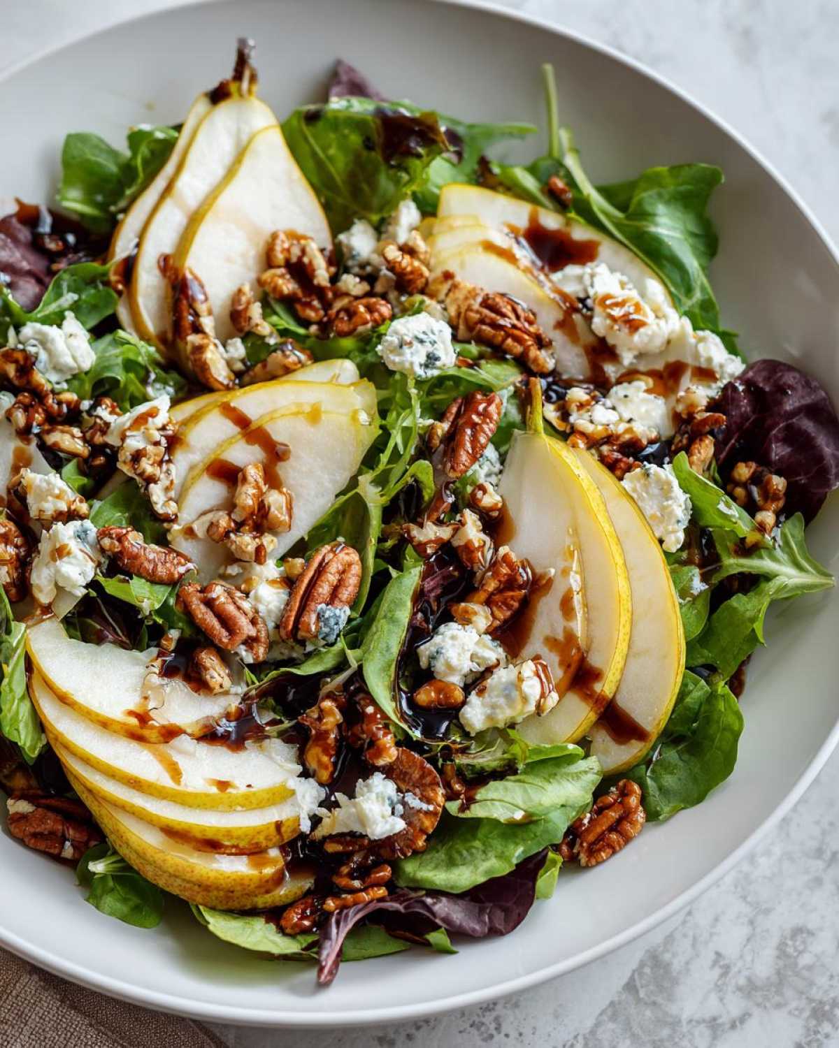Close-up of a vibrant pear salad featuring sliced pears, blue cheese crumbles, pecans, and a balsamic glaze over mixed greens.