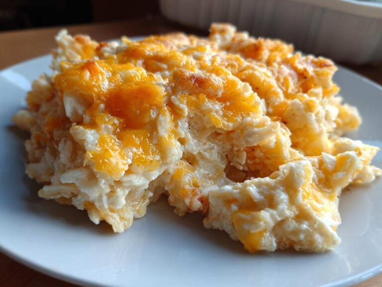 A close-up serving of creamy, cheesy hashbrown casserole topped with melted orange cheddar cheese.