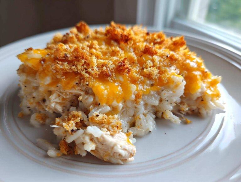 A close-up serving of creamy chicken and rice casserole topped with melted cheddar cheese and crunchy breadcrumbs.