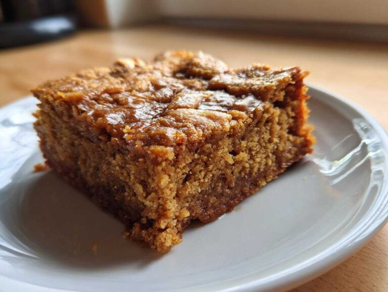 Close-up of a single, moist square of banana bread blondies with a rich, golden-brown top, served on a white plate.