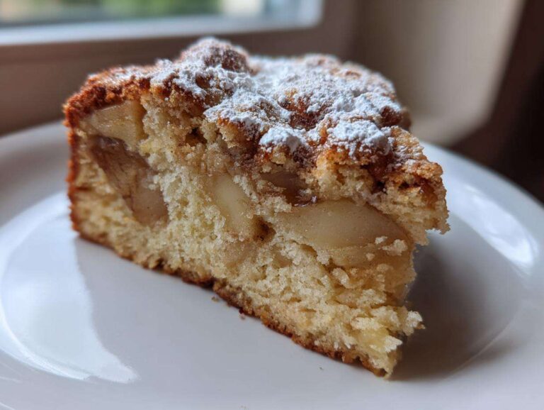A close-up of a moist slice of easy cinnamon apple cake topped with powdered sugar on a white plate.