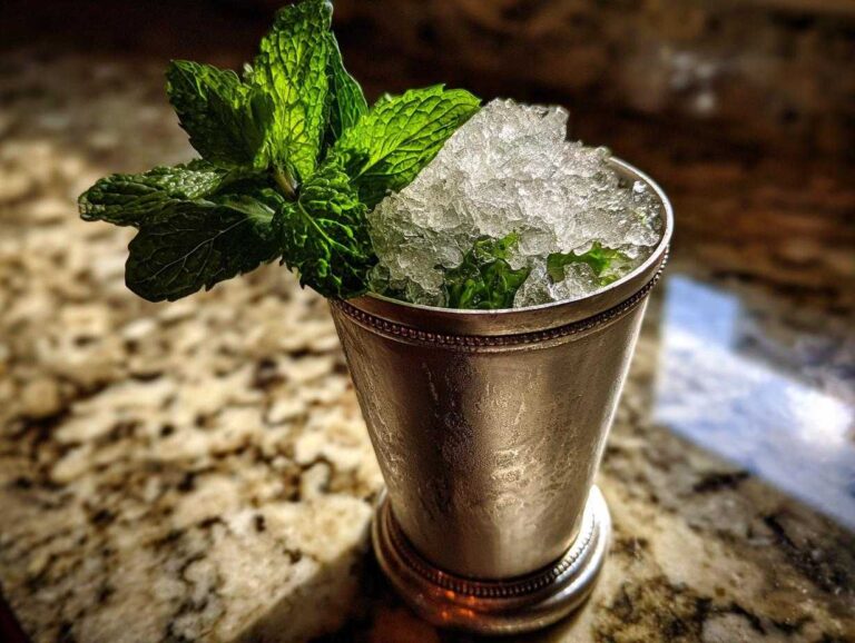 A classic Mint Julep cocktail served in a frosted silver julep cup, topped high with crushed ice and a large sprig of fresh mint.