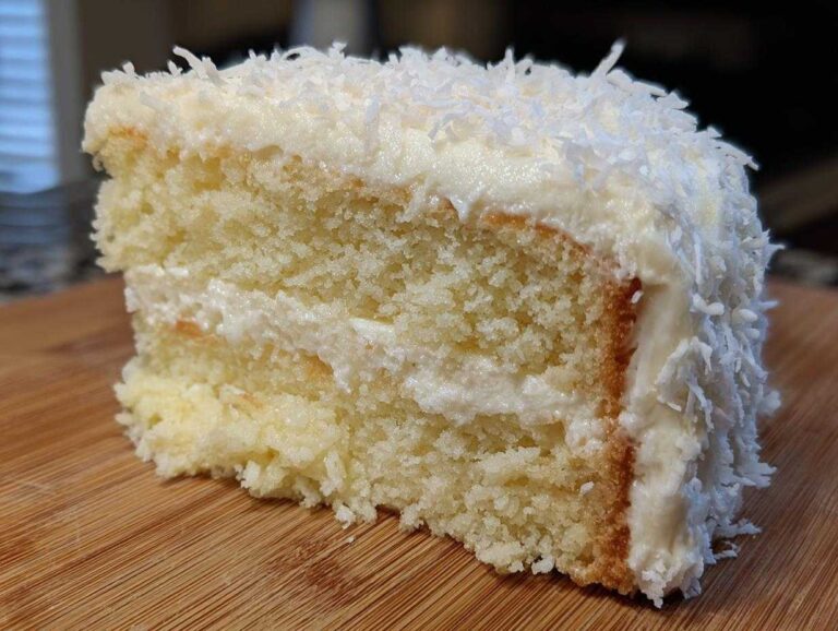Close-up of a moist slice of three-layer coconut cake covered in white frosting and shredded coconut.