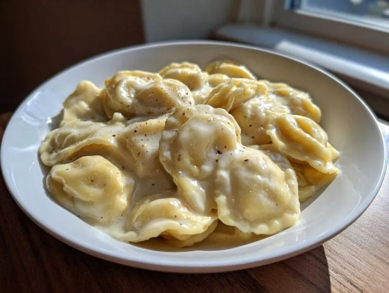 Close-up of ravioli generously coated in a rich creamy ravioli sauce, topped with black pepper.