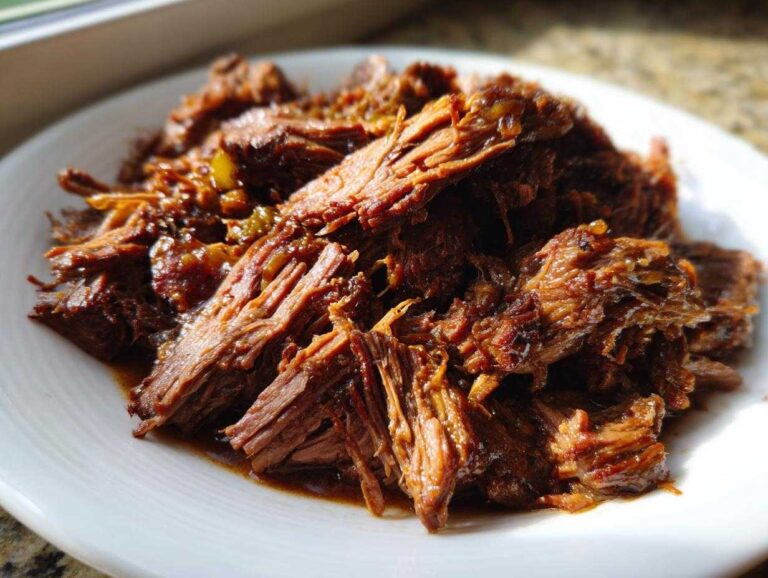 Close-up of tender, shredded Mississippi Pot Roast served on a white plate with rich juices.