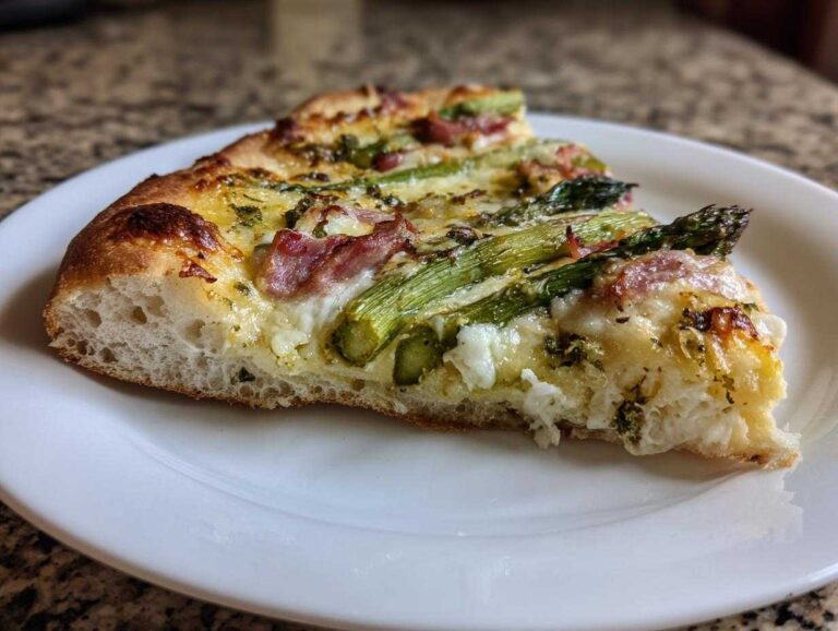 Close-up of a slice of Asparagus White Pizza showing thick crust, melted cheese, asparagus spears, and bits of prosciutto.