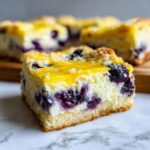 Close-up of a rich slice of blueberry cheesecake bars with lemon glaze topping on marble.