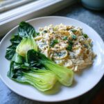 A serving of creamy Cabbage alfredo with sautéed bok choy on a white plate, garnished with pepper and green onions.