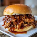 Close-up of a delicious sandwich filled with saucy Crockpot pulled pork for sliders on a soft brioche bun.