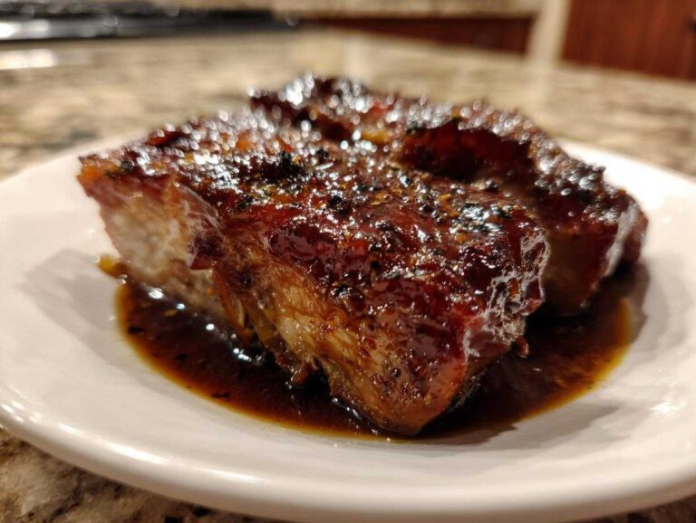 Close-up of a piece of glazed, dark meat served in a rich sauce, potentially alongside braised cabbage with ginger and garlic.
