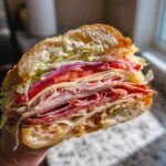 Close-up of a heavily loaded Graduation party sub sandwiches, showing layers of deli meats, cheese, lettuce, tomato, and onion.