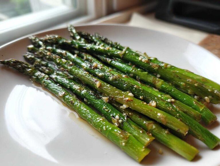 A serving of bright green roasted asparagus with lemon and garlic bits on a white plate.