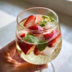 Close-up of a glass filled with Strawberry mint sangria, showing sliced strawberries, mint leaves, and ice cubes.